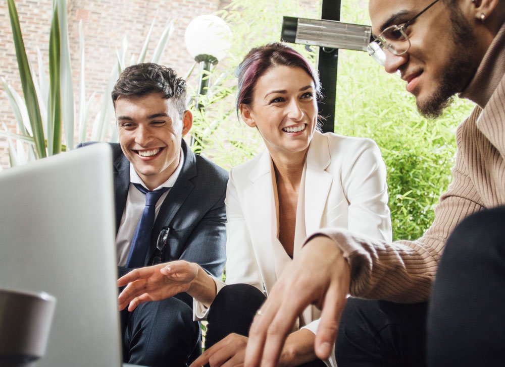 3 people smiling together while working on computer